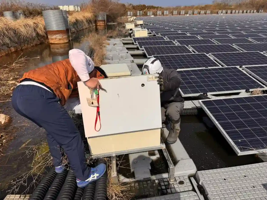 青空の下で住宅の屋根に設置された太陽光パネルとパワーコンディショナの点検イメージ